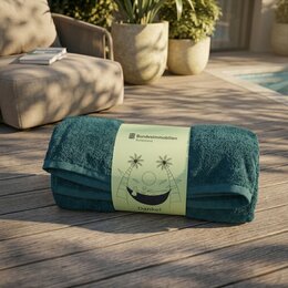 Gerolltes petrolfarbenes Frottier-Handtuch als Werbemittel mit BundesImmobilien-Logo und passender Banderole auf einer Terrasse.