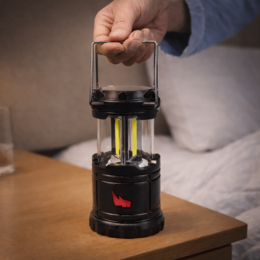 Schwarze LED-Campinglampe als Werbeartikel mit rotem Logodruck, gehalten am Metallbügel über einem Tisch.