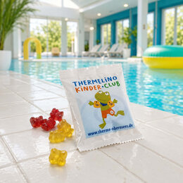 Eine Fruchtgummitüte mit Frosch-Maskottchen des Thermelino Kinder-Clubs und ein paar Gummibärchen werden in einem Schwimmbad am Beckenrand dargestellt.