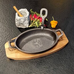 Iron Plate Gusseisenpfanne mit Logo-Brandstempel in dekorativer Food-Präsentation auf Servierplatte aus Akazienholz mit schwarzem Hintergrund