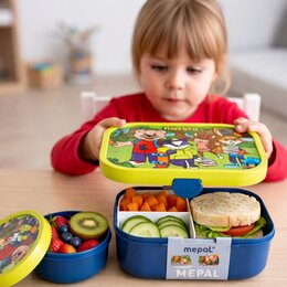 Kind öffnet eine gefüllte Mepal Brotdose mit bedrucktem Deckel. Daneben steht eine passende Fruchtbox mit Beeren und Kiwi.