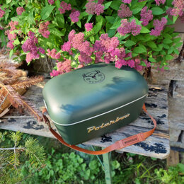 Grüne Retro-Kühlbox Polarbox mit Wuiderer-Logo auf Deckel und Lederriemen auf Holztbank im Garten