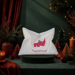 Traubenkernkissen mit Augustinum-Logo bedruckt auf grünem Samtpodest in festlicher Weihnachtsdekoration mit Kerzenlicht und Tannenzweigen
